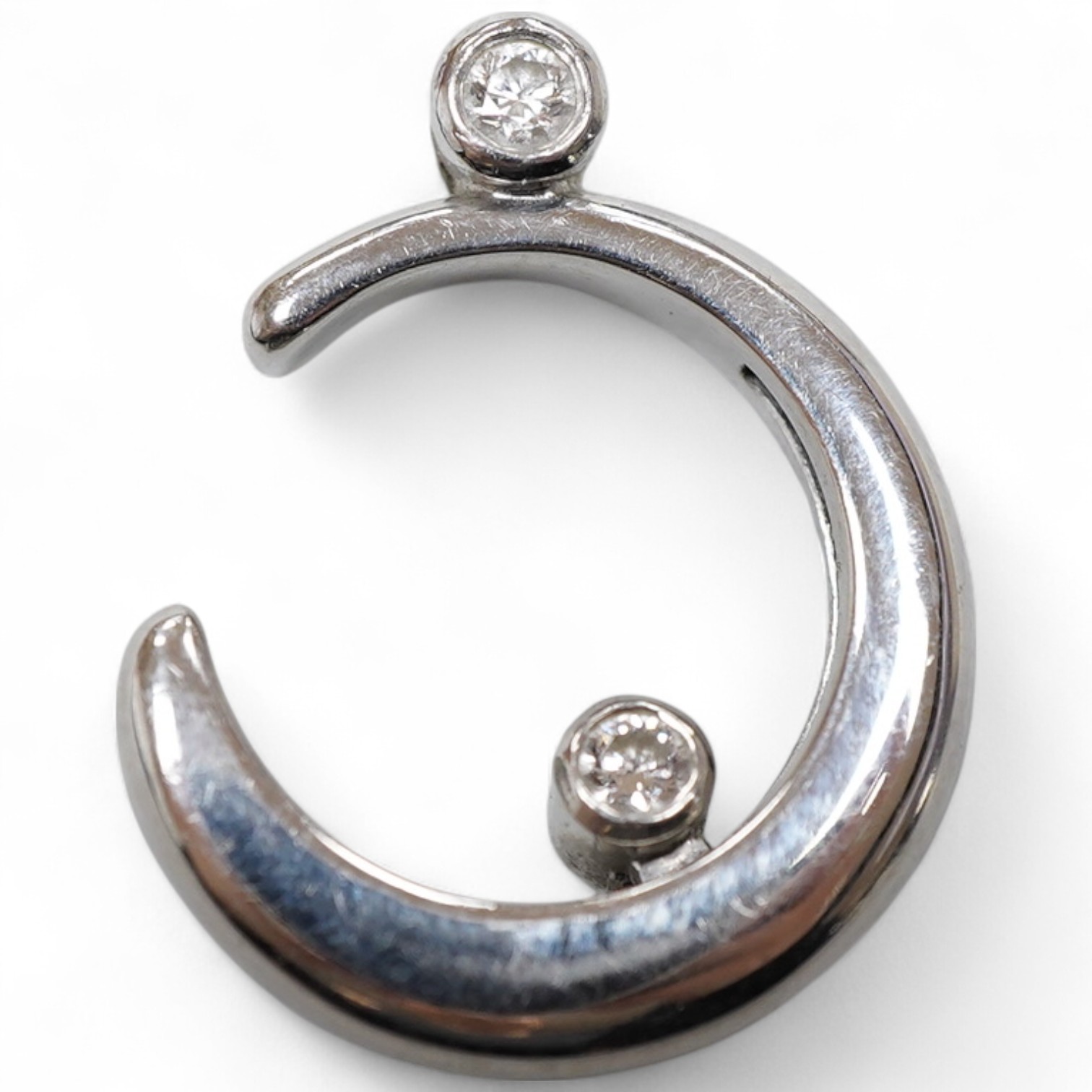 A diamond pendant, designed as a crescent moon accented with two collet-set brilliant-cut diamonds totalling approximately 0.20 carats, one sliding up and down the inner curve of the moon, length 2.6cm, mounted in platin